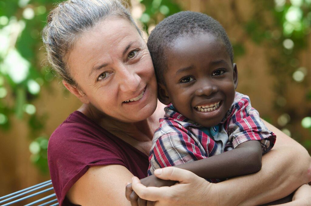 Kuvassa vaaleaihoinen nainen pitää tummaihoista lasta sylissä ja molemmat hymyilevät.